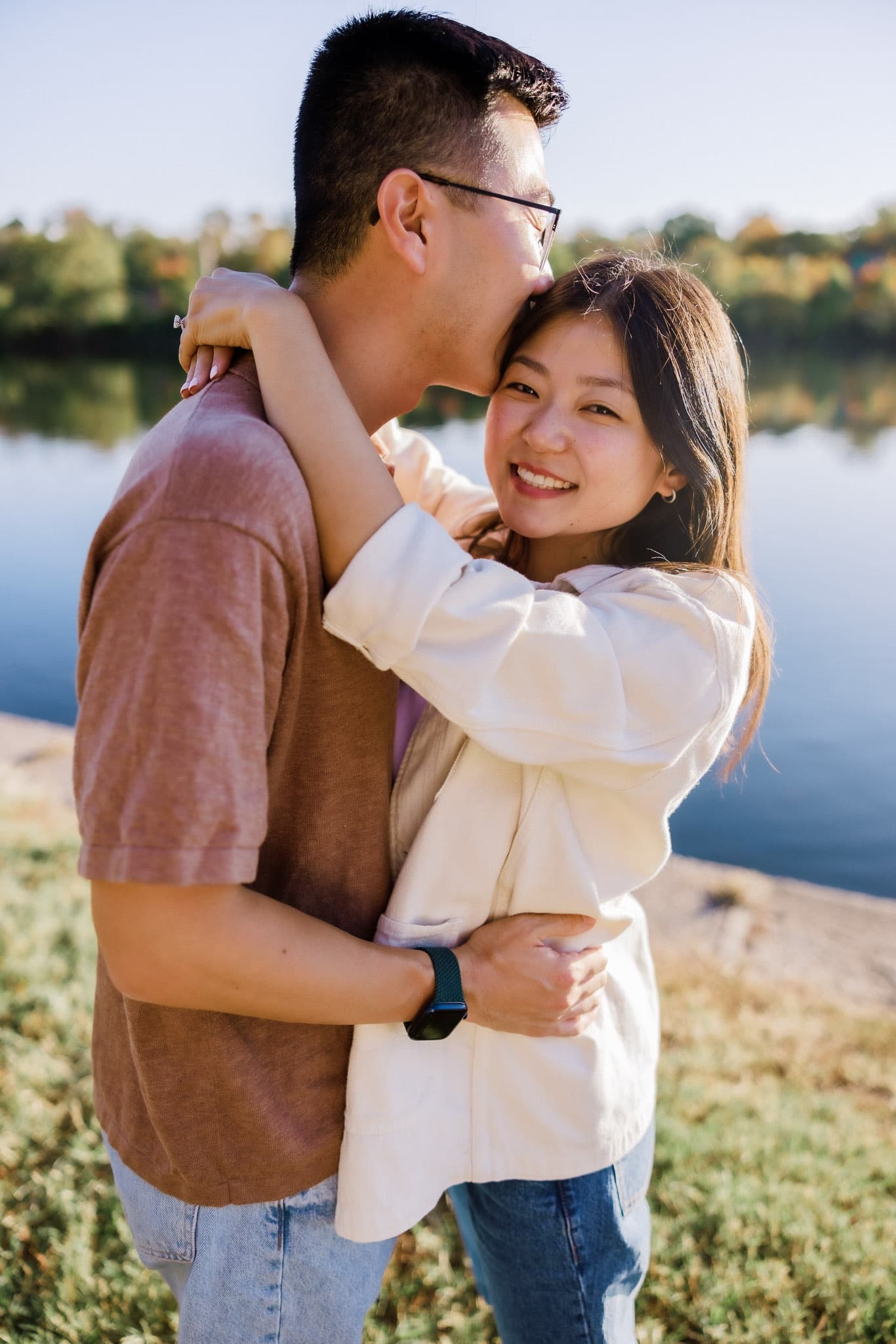 Couple laughing in a warm embrace beside a sunlit lake